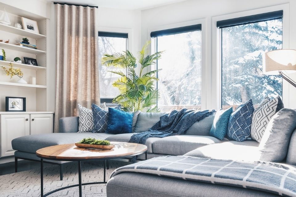 Natural light flows through the window in this living room with a gray couch and wooden coffee table 